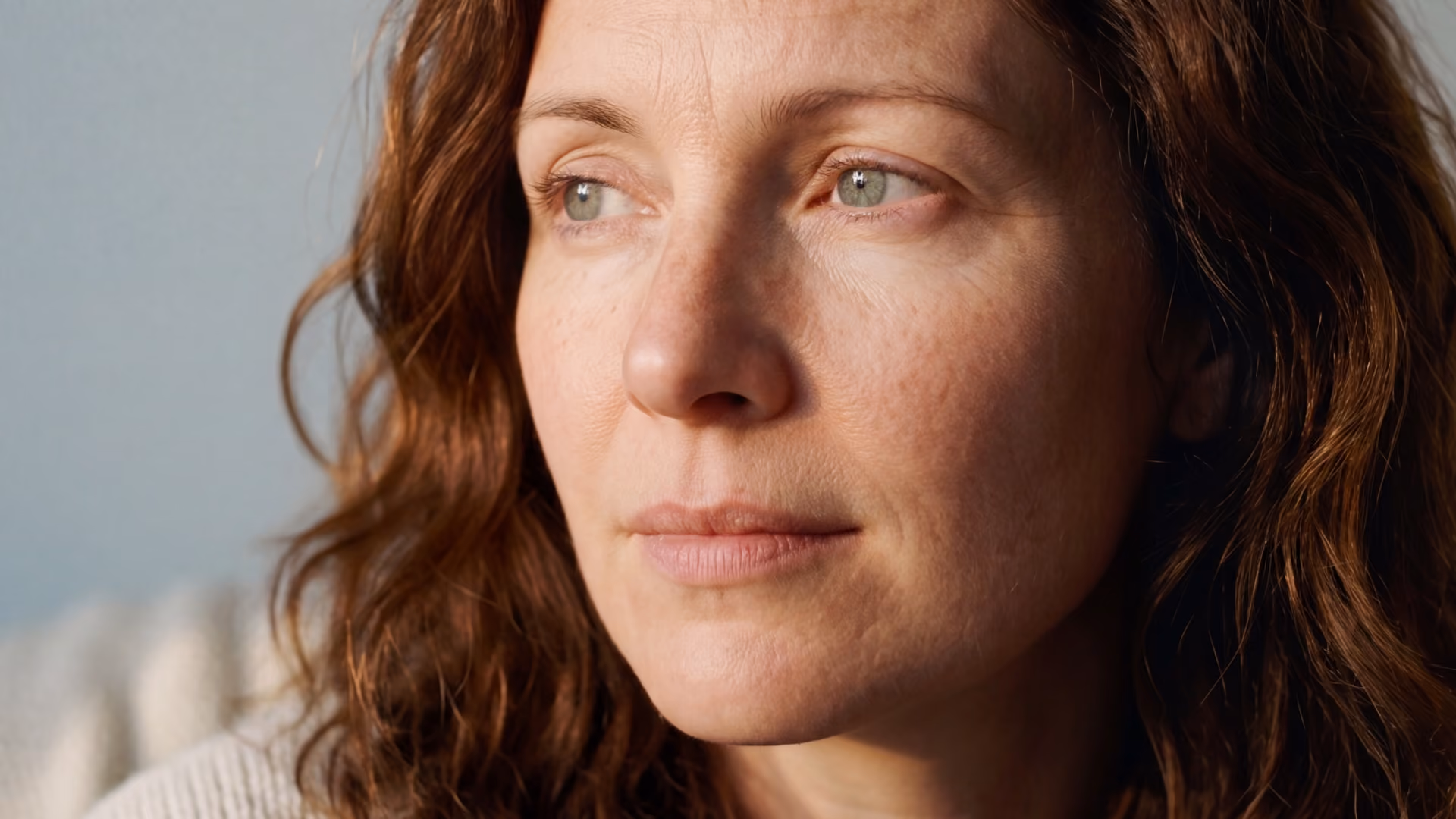 A redheaded white woman looking thoughtful, representing difficulty reaching orgasm, or anorgasmia, and how it can be treated