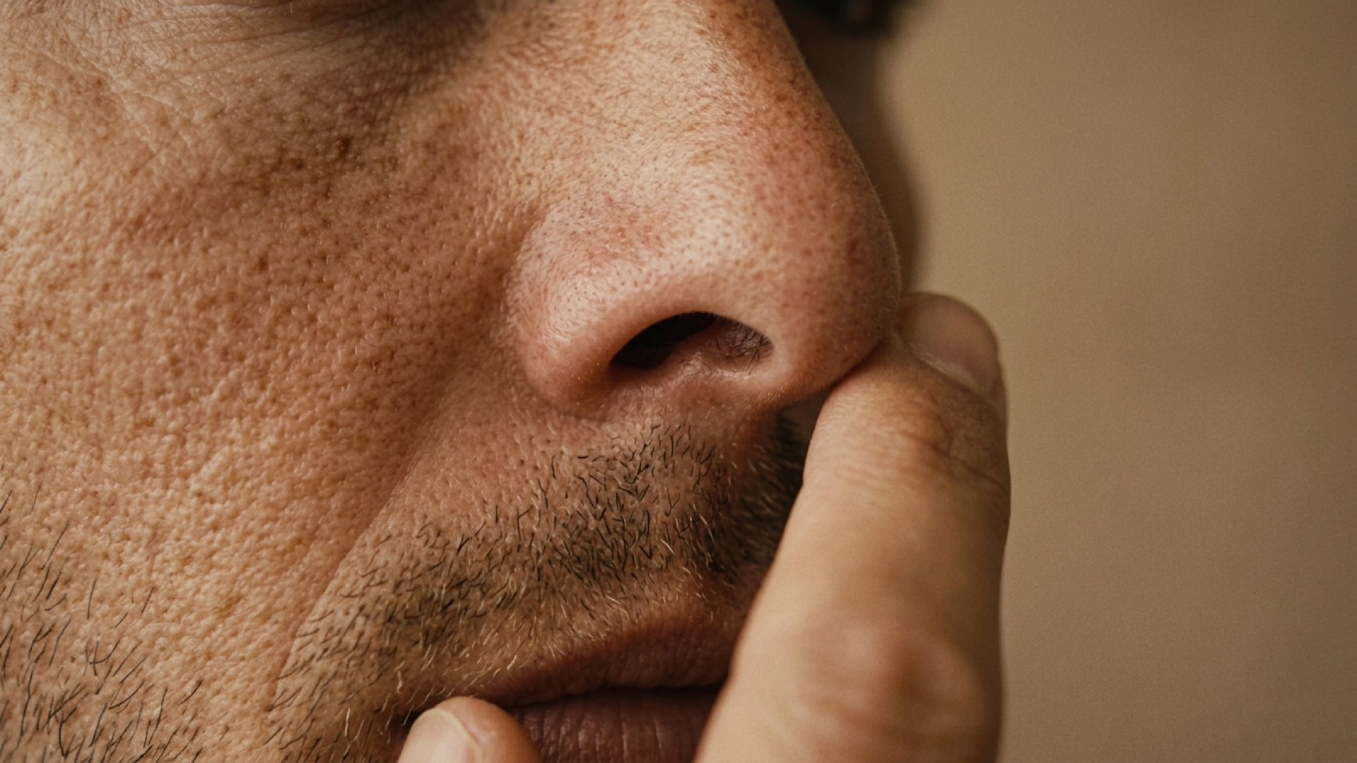 A close up of a white man's nose. He has his hand to his face, thinking.