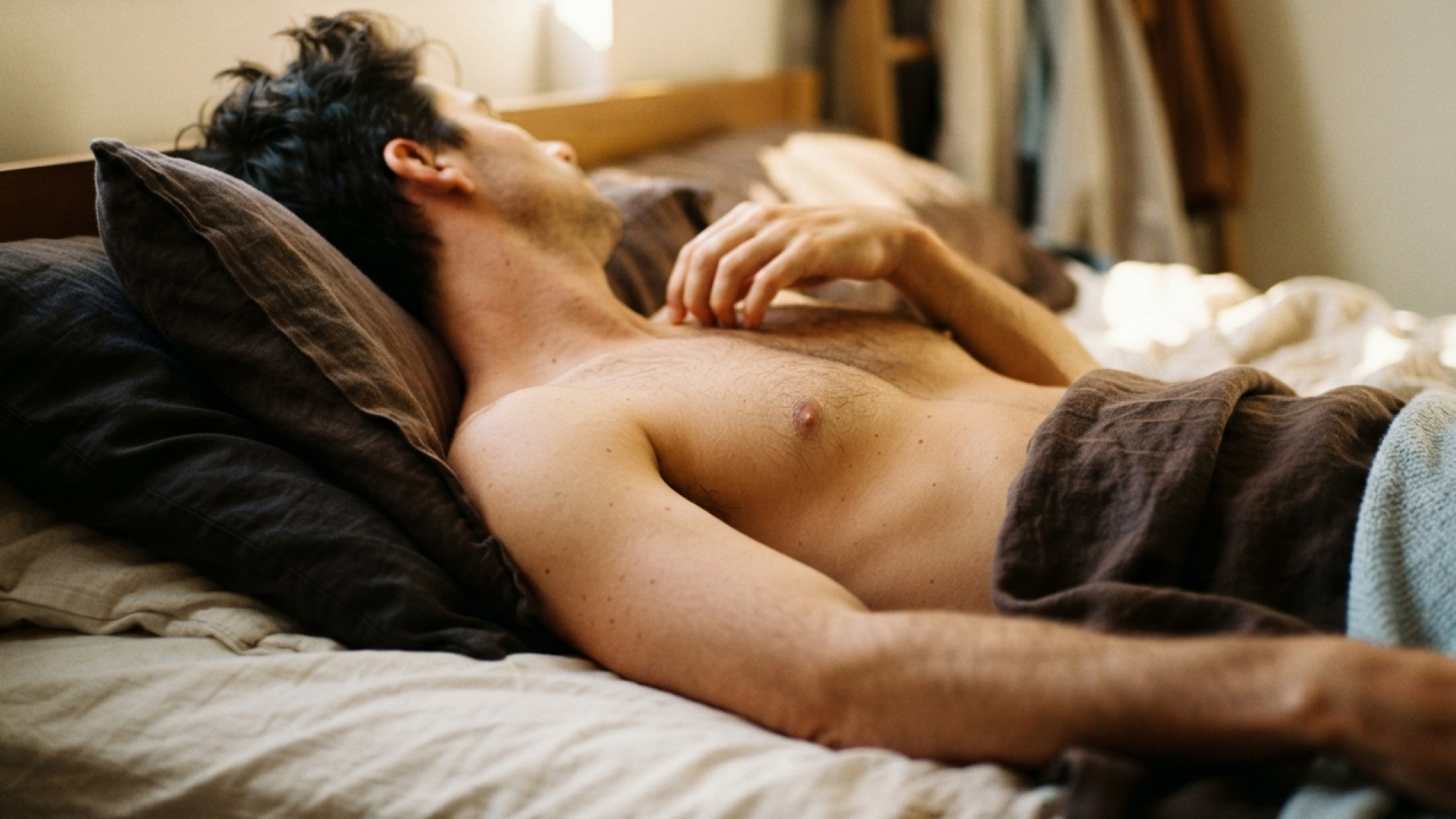 A white man lies in bed looking away from the camera