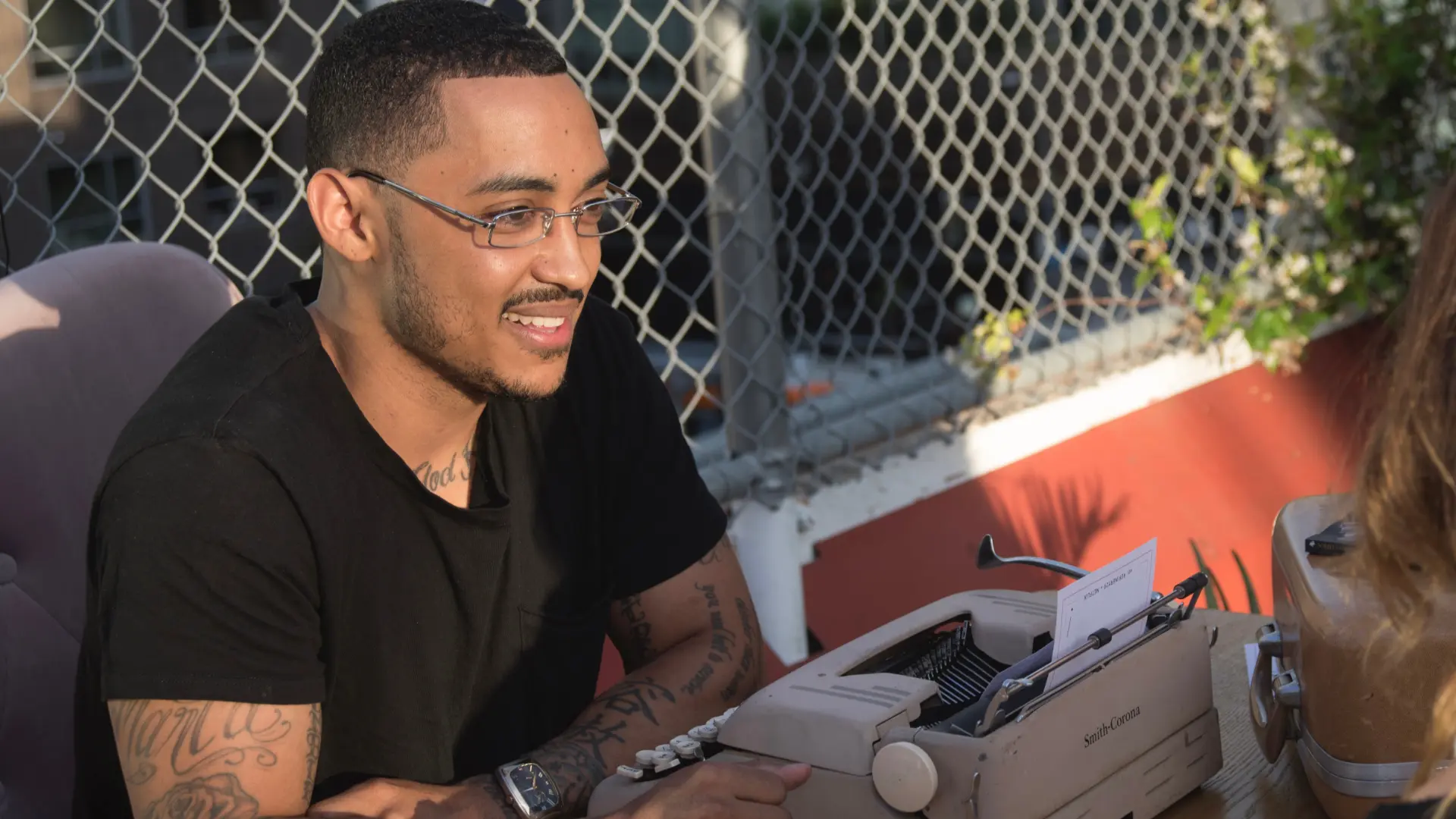 Andre smiling as he sits at a vintage typewriter on a sunny rooftop
