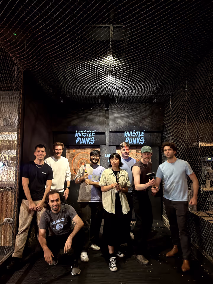 Seven people posing inside an axe-throwing venue in front of two targets labeled Whistle Punks, some holding axes or tools used for throwing.