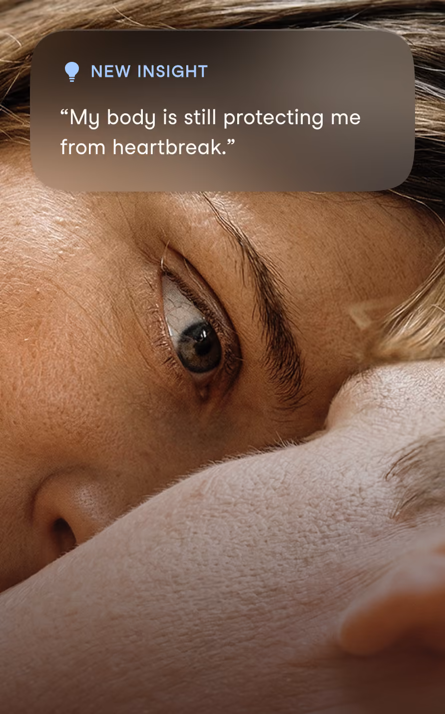 Close-up of a person's face lying down, showing one eye looking forward, with an overlay text reading, New Insight: “My body is still protecting me from heartbreak.”