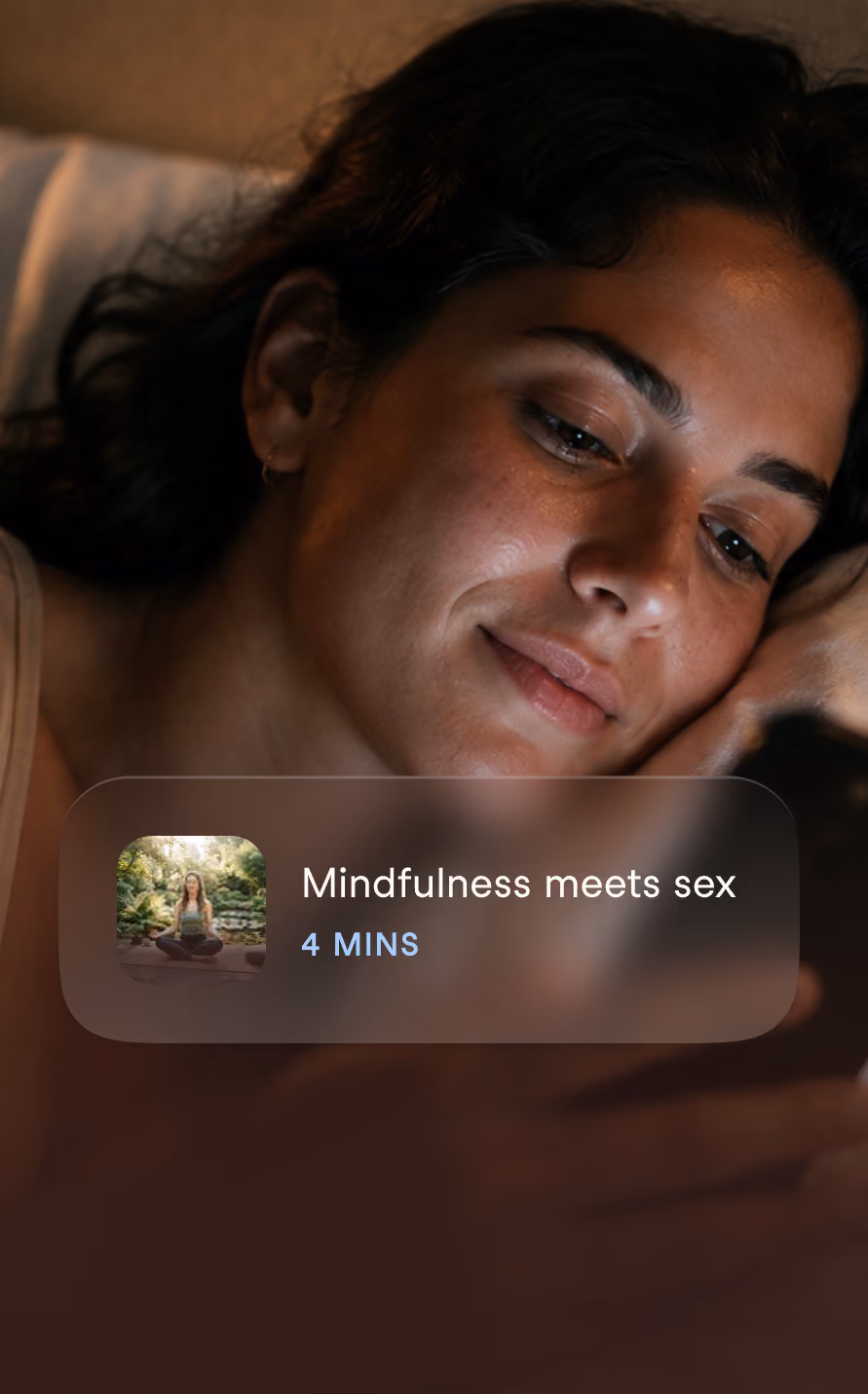 Close-up of a woman with dark hair lying down and looking at a softly glowing screen with a relaxed smile; a translucent overlay on the image reads 'Mindfulness meets sex' with a duration of '4 MINS' and a small thumbnail of a person meditating in a garden.