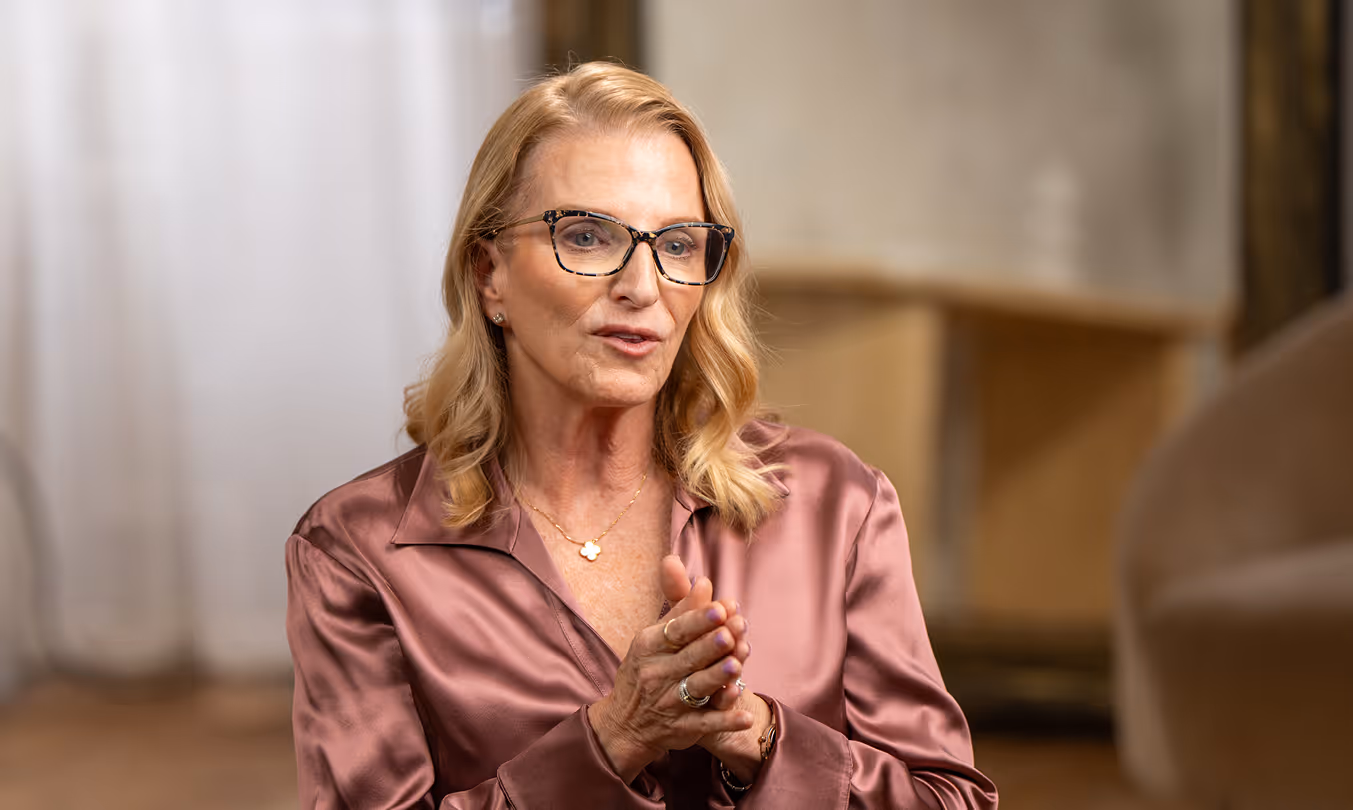 Dr. Suzette Johnson, board-certified OBGYN, with blonde hair and glasses in a rose satin blouse, speaking to camera