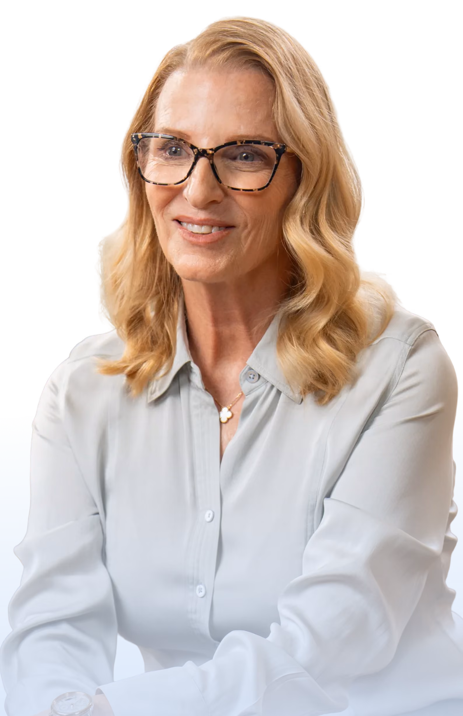 Smiling middle-aged woman with wavy blonde hair wearing tortoiseshell glasses and a light grey buttoned shirt.