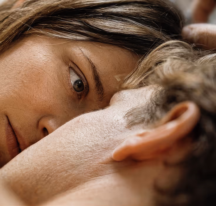 Close-up of a woman and a man lying down with their heads close, looking intently at each other.